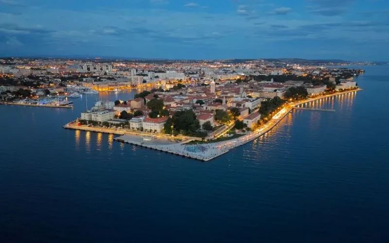 Stunning aerial view of Zadar's illuminated coast at twilight, showing the vibrant cityscape.