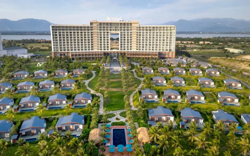 Aerial view of a luxury resort with bungalows surrounded by mountains and palm trees.