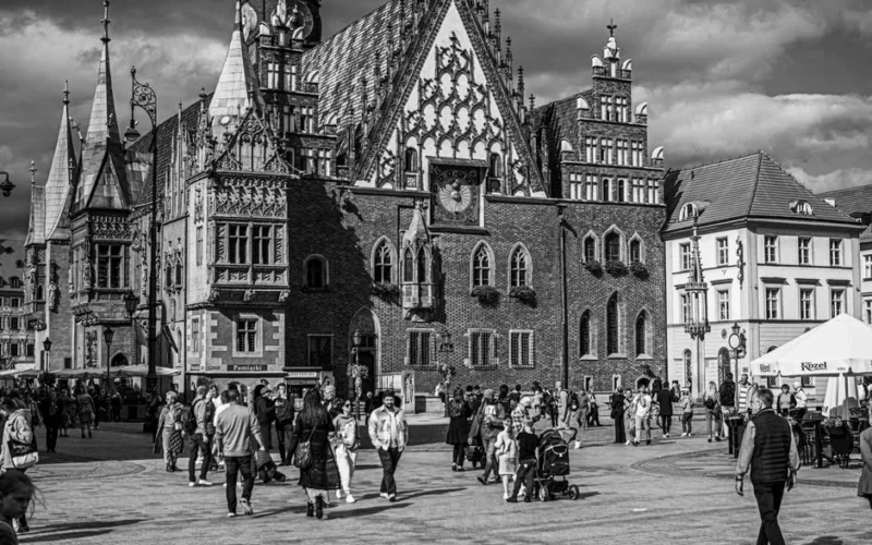 Black and white photo of a bustling historic square with Gothic buildings and people.