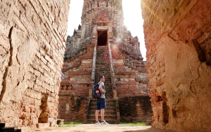 A man with a backpack sightseeing ancient brick temple in summer sunlight.