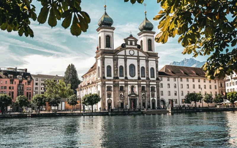 Beautiful capture of the Jesuit Church on Lucerne's waterfront with a picturesque mountain backdrop.