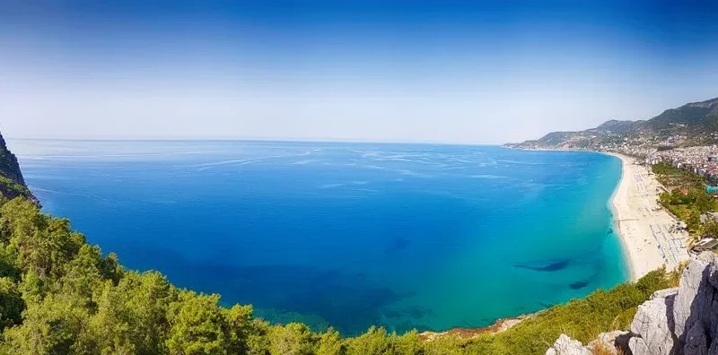 Stunning panoramic view of Alanya's turquoise coastline, beach, and distant cityscape in Antalya, Turkey.