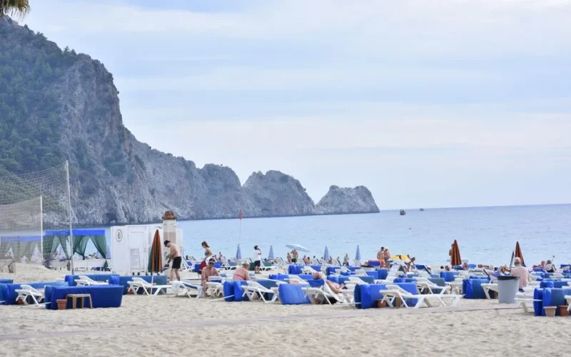 Beautiful sandy beach in Alanya, Turkey with sun loungers and scenic rocky cliffs.