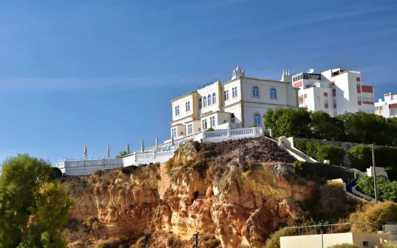Elegant villa on a rocky Algarve cliff with clear blue skies in Faro District, Portugal.
