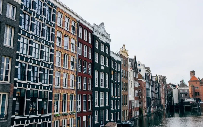 Exterior of narrow multicolored apartment houses without balconies overseeing canal with modern boats moored near entrances