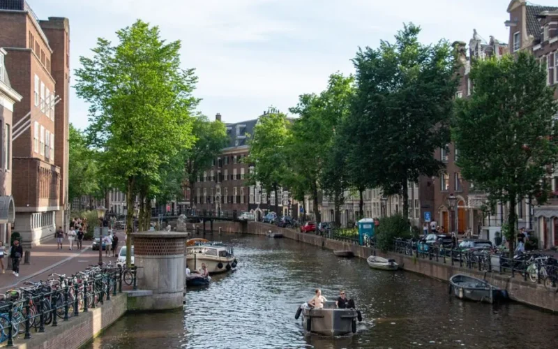 Explore the scenic Amsterdam canal with boats and historic buildings lining the water.