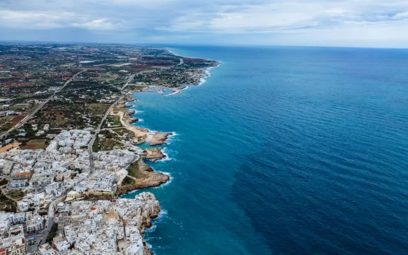 Breathtaking aerial view of Polignano a Mare's coastline in Italy, showcasing vibrant blue waters and summer vibes.