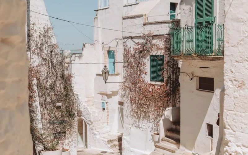 Explore the picturesque alleys of Ostuni, Apulia, with sunlit whitewashed buildings and green shutters.