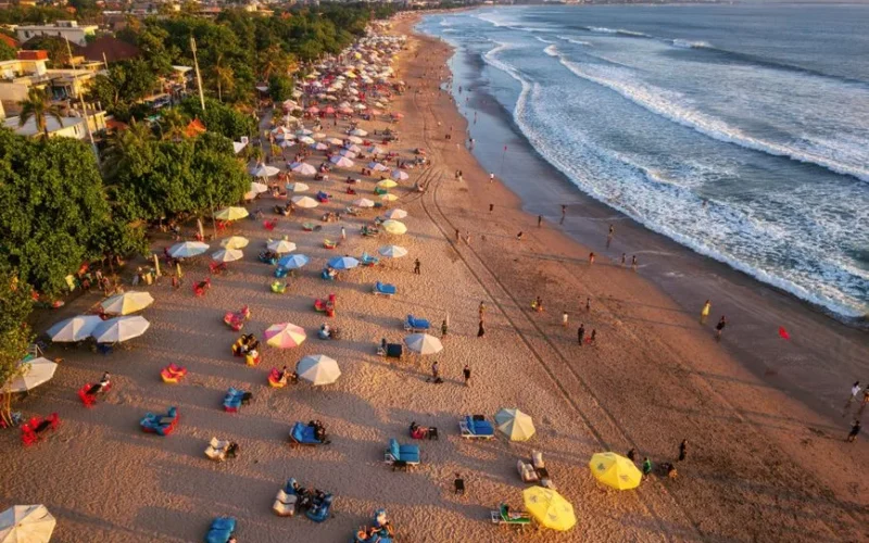 Aerial shot of lively beach with colorful umbrellas and ocean waves in Bali, Indonesia.