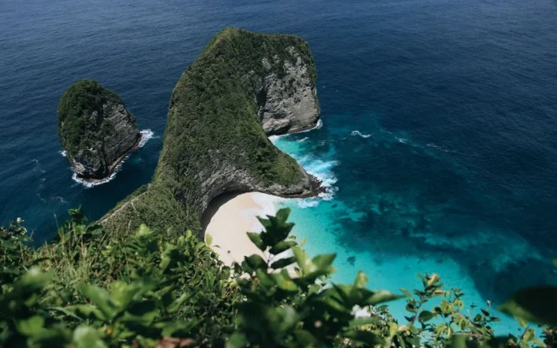 Stunning aerial view of Nusa Penida's picturesque beach in Bali surrounded by clear turquoise waters and lush green cliffs.