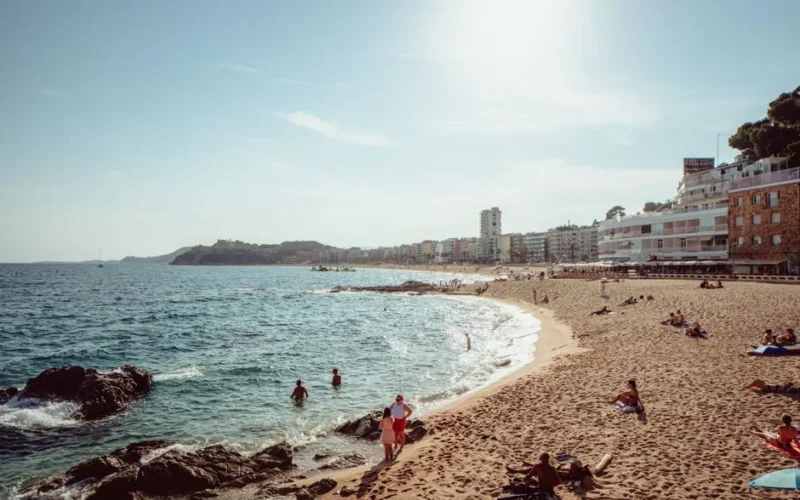 A vibrant beach scene at Lloret de Mar, Spain, with people enjoying the sun and sea.