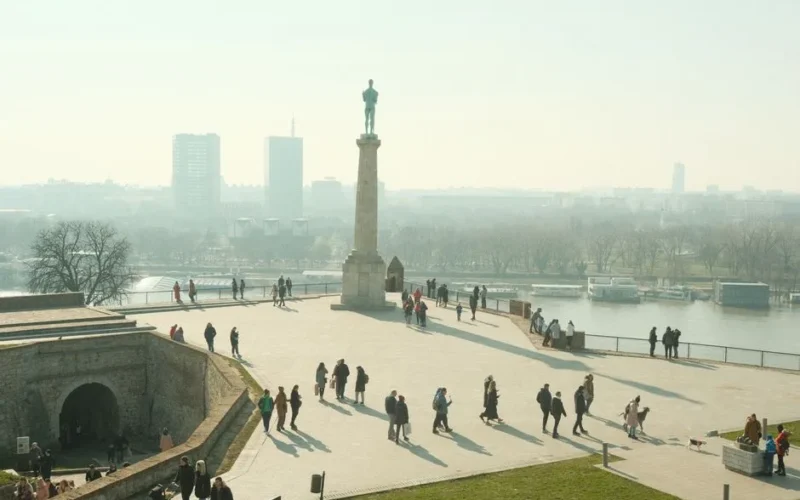 Scenic view from Belgrade Fortress overlooking the city and river, people walking in the plaza.