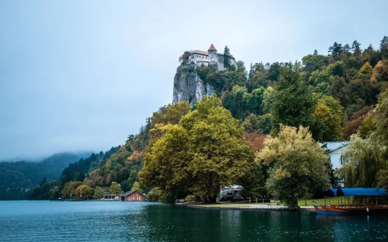 Bled Castle perched on a clifftop with serene lake and lush forest surroundings, offering a picturesque view.