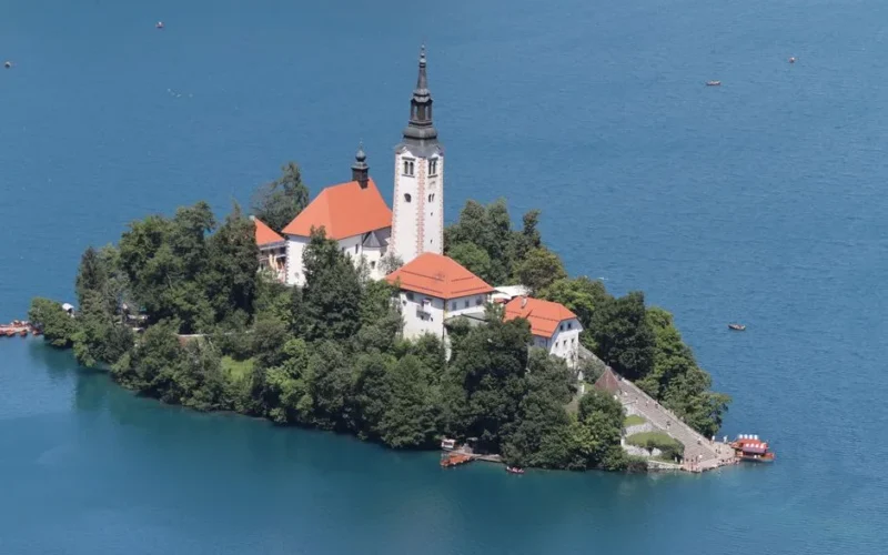 Stunning aerial view of Bled Island and church on Lake Bled, Slovenia, surrounded by crystal blue water and lush greenery.