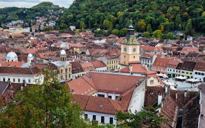 Scenic aerial view of Brașov’s historic old town with iconic Clock Tower and lush green hills.
