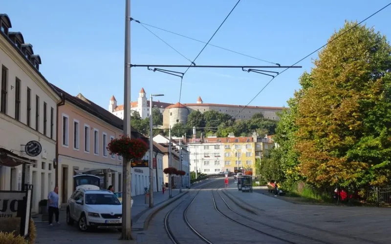 Street view of Bratislava with tram tracks and the iconic Bratislava Castle in the background.