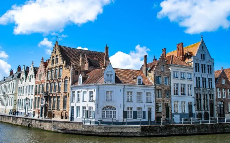 Charming townhouses along a canal in Bruges, Belgium under a vibrant blue sky.