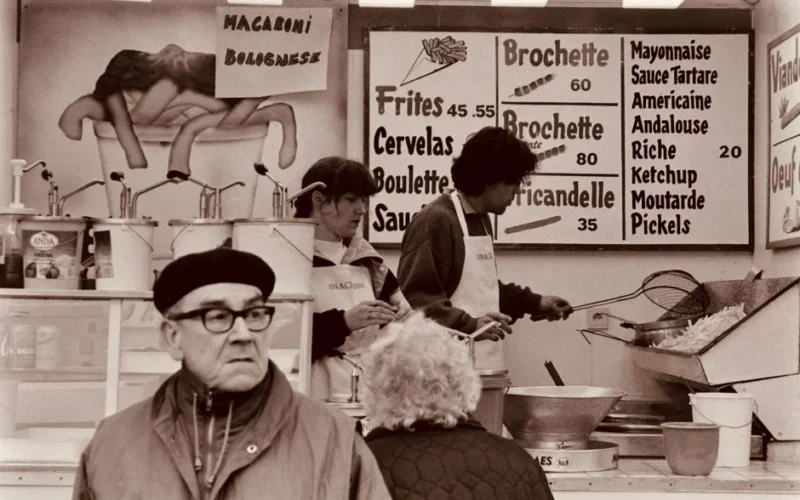 Vintage capture of a Belgian food stall with people preparing and ordering food in Nivelles.