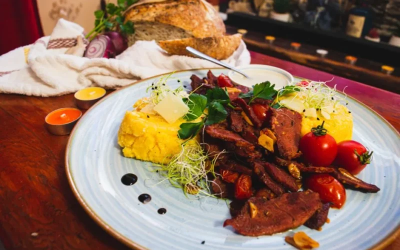 Savor a traditional Romanian meal featuring juicy beef, polenta, and fresh vegetables, perfect for a culinary adventure.