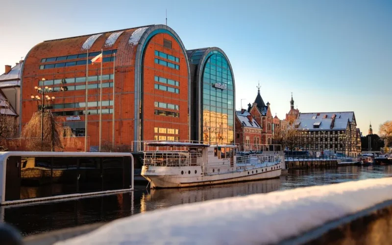 A picturesque winter scene in Bydgoszcz, Poland, featuring the iconic granaries along the Brda River with a boat docked nearby.