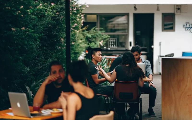 Young adults in a relaxed outdoor café setting in Belo Horizonte, engaging in conversation and work.