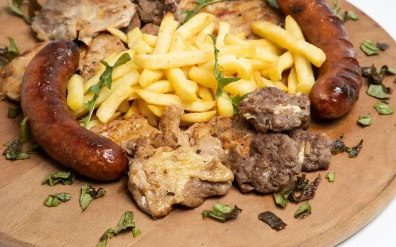 Tasty assortment of grilled meats and French fries on a rustic wooden board.