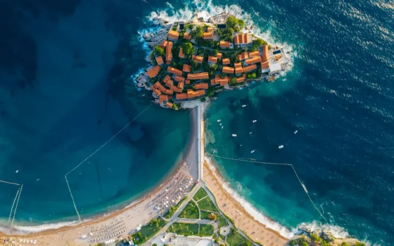 Stunning aerial photo of a coastal island with turquoise waters and vibrant roofed buildings.