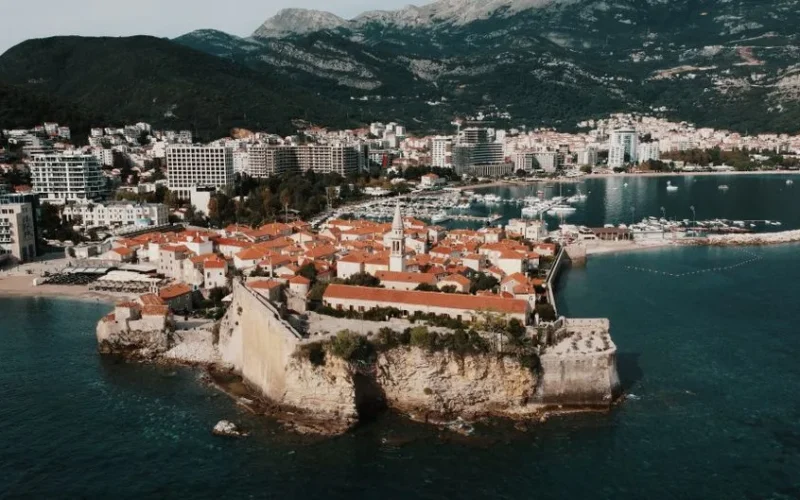 Drone capture of Budva Old Town with red roofs and Adriatic Sea, showcasing Montenegro's coastal beauty.