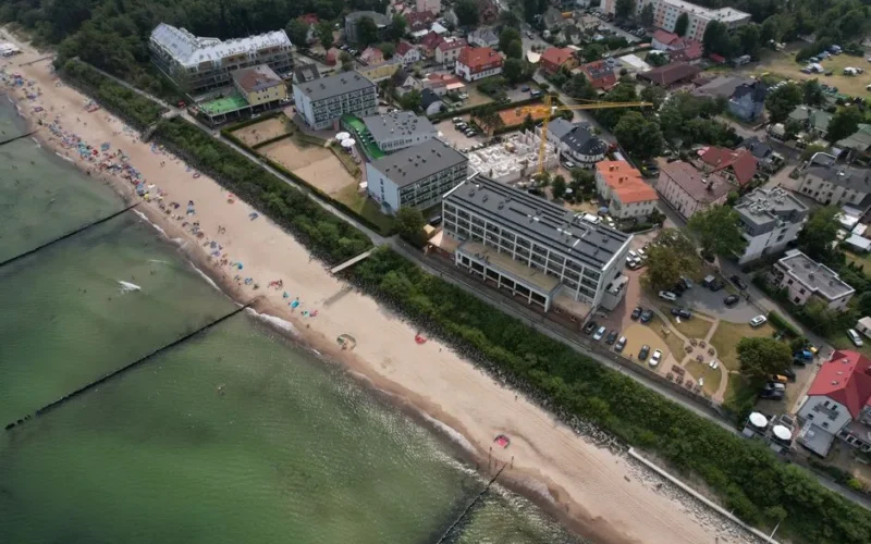 Aerial shot capturing a town along a sandy beach by the ocean, featuring buildings and greenery.