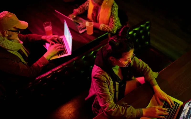 Above view of three adults using laptops in a cozy cafe with vibrant lighting.