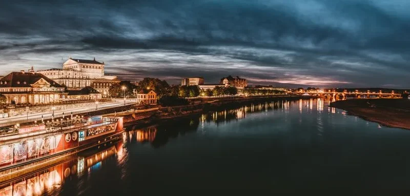 Stunning dusk view of an illuminated city skyline reflected on a river, showcasing urban beauty.