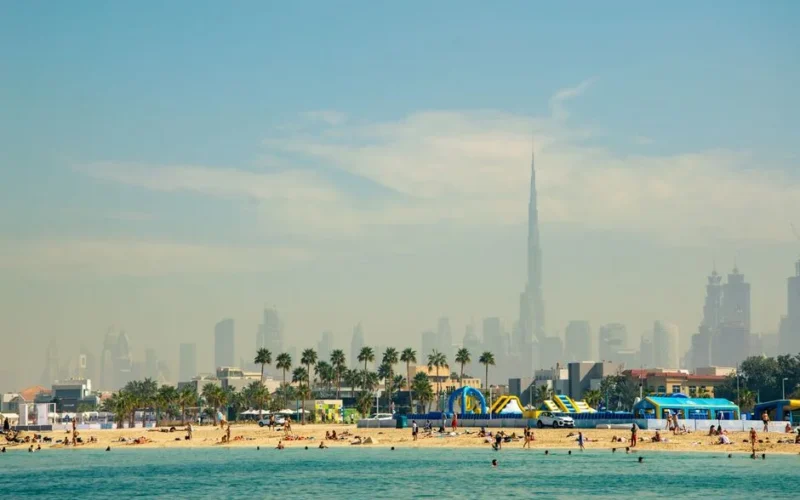 Tourists enjoying a sunny day at Dubai beach with Burj Khalifa and skyline in the background.