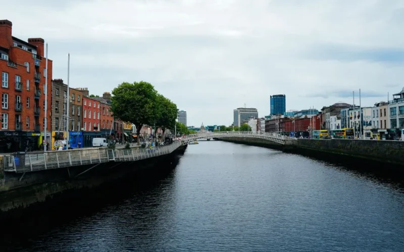 Scenic view of Dublin's Ha'penny Bridge over the River Liffey amidst urban architecture and vibrant city life.