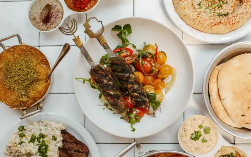 Delicious Middle Eastern spread featuring kebabs, dips, hummus, and traditional breads on a white ceramic background.