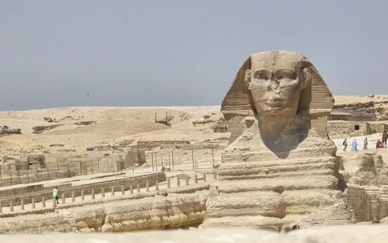 A clear daytime view of the Great Sphinx of Giza, Egypt, surrounded by sandy desert.