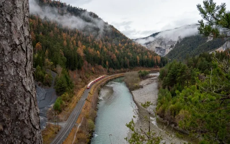 A scenic view of a train winding through the picturesque Safiental Valley in Switzerland during autumn.
