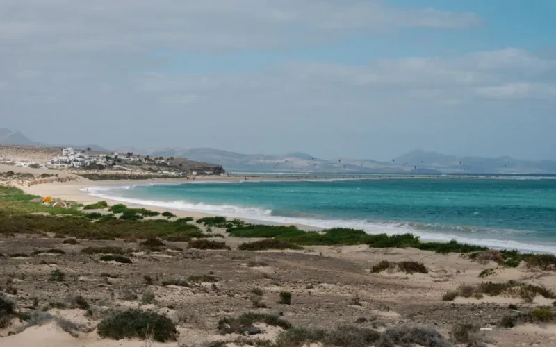 Beautiful landscape of a coastal area with turquoise ocean, sandy beach, and distant mountains.