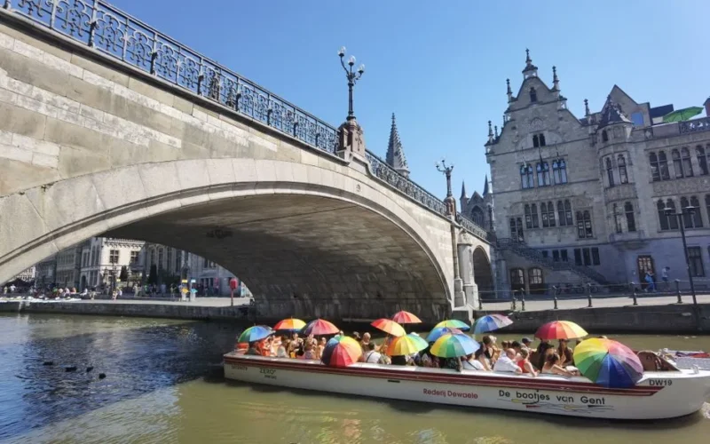 Vibrant boat ride under St. Michael's Bridge in Ghent, Belgium with rainbow umbrellas and historic architecture.