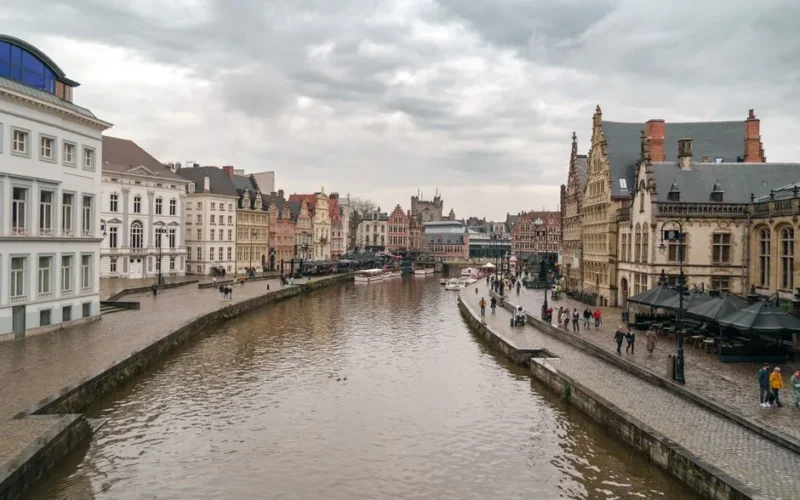 Charming canal scene in Ghent, Belgium with historical architecture on a cloudy day.