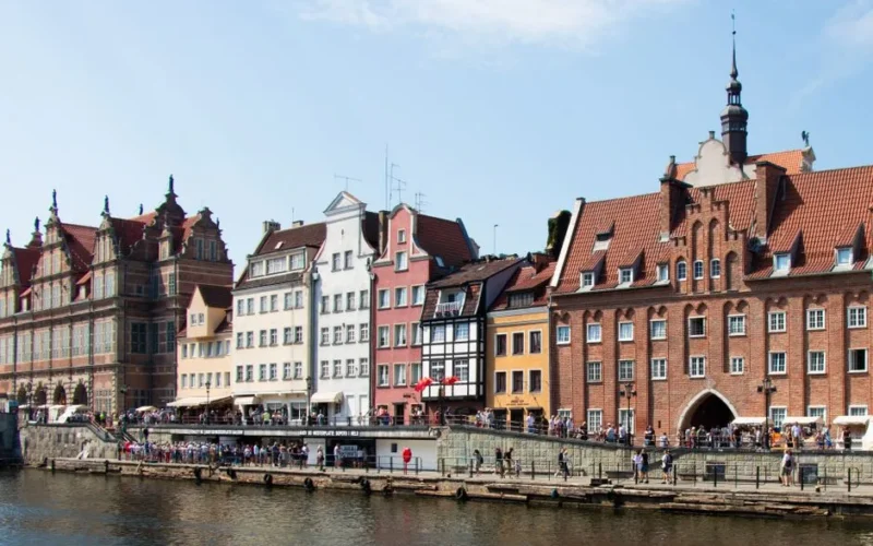 Charming view of Gdańsk's historic waterfront lined with colorful buildings and lively visitors.