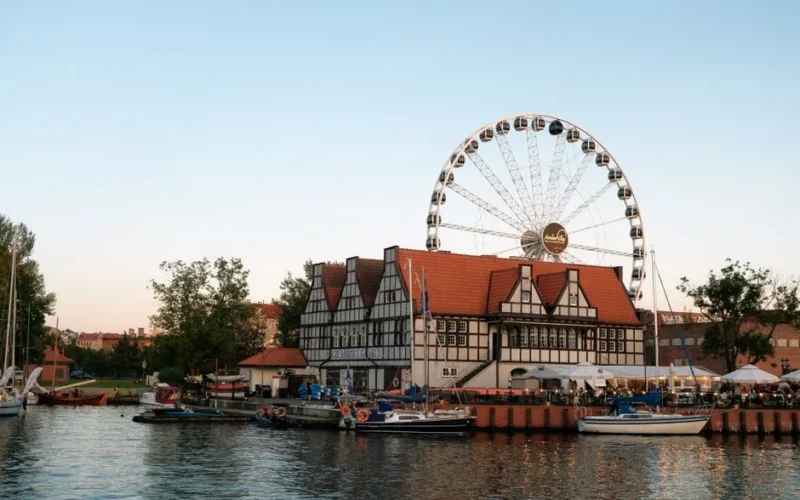 Charming evening view of the Ferris wheel and historic buildings by the water in Gdańsk, Poland.