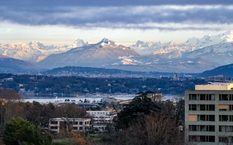 A breathtaking view of Geneva with Swiss Alps backdrop under a cloudy sky at day.