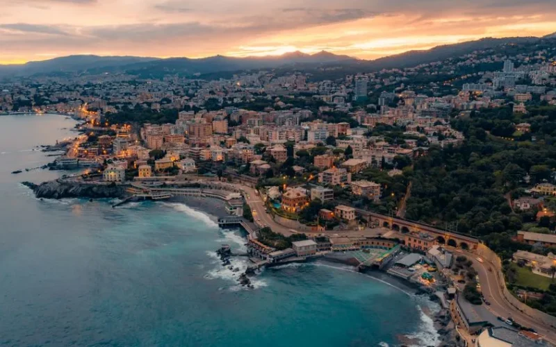 Stunning aerial view of Genoa's waterfront and cityscape at sunset, showcasing vibrant colors and coastal beauty.