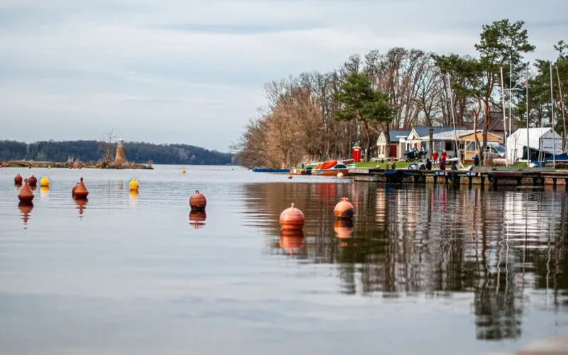 Peaceful lakeside scene with buoys and boats docked by a waterfront on a calm day.