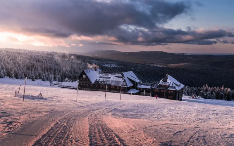 A scenic view of a snow-covered mountain lodge surrounded by winter forests at sunrise.
