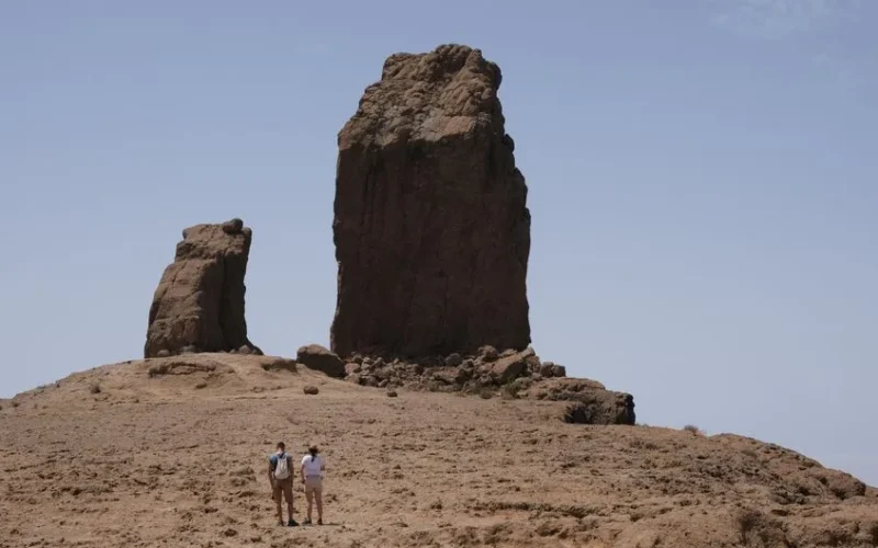 Two hikers explore the iconic Roque Nublo rock formation under clear skies in Gran Canaria, Spain.