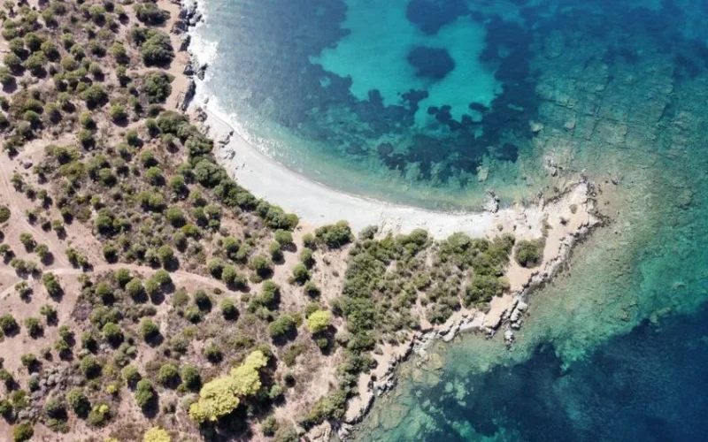 A stunning aerial shot of a Greek coastline with clear blue waters and lush greenery.