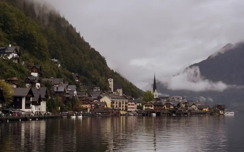 Picturesque village by the lake with misty mountains and charming architecture on a cloudy day.