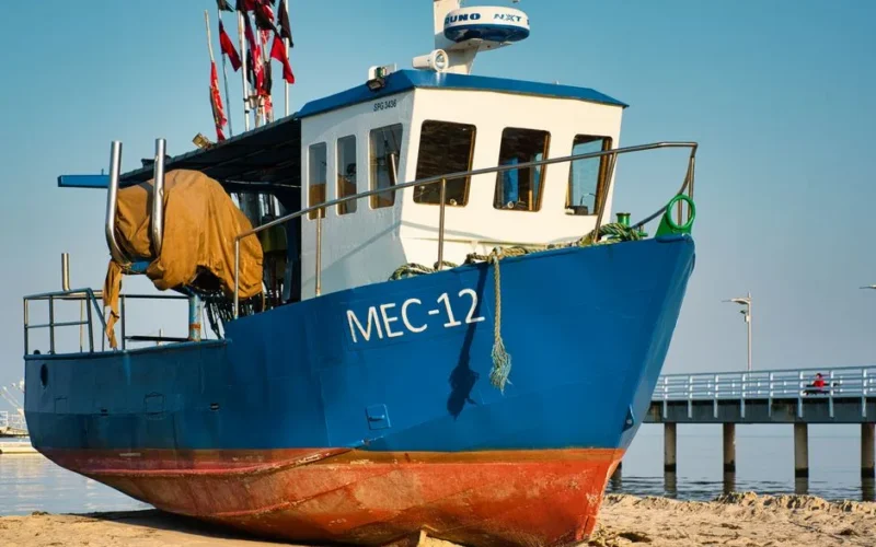 Colorful fishing boat MEC-12 resting on the sandy shore by a pier in Poland.