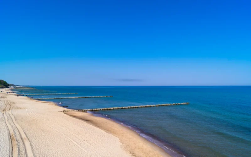 A stunning aerial view of Ustronie Morskie's sandy beach and blue sea under a clear summer sky.